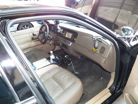 2003 Ford Crown Victoria - Driver-side view of a tan interior with sport wheel, center display and floor-mounted electronics.
