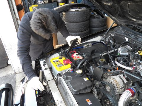 2003 Ford Crown Victoria - Technician leans into an engine bay with a yellow battery and blue ignition wires.