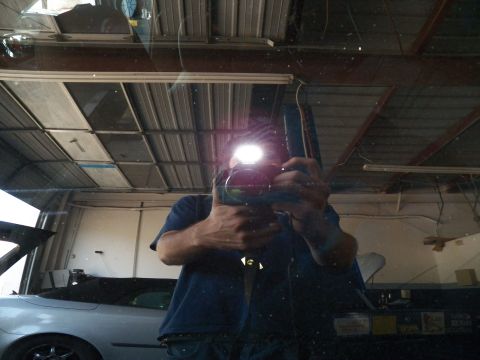 2003 Ford Crown Victoria - Camera-with-flash self-reflection captured in a car's glass inside a service garage with silver car in background