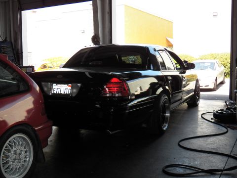 2003 Ford Crown Victoria - Lowered black sedan with EVL VTC plate parked in a garage bay next to a red hatchback and air hose