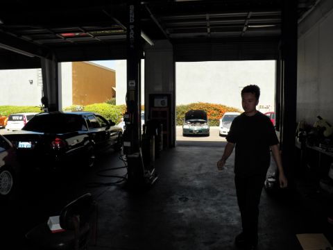 2003 Ford Crown Victoria - Person stands inside a shadowed repair shop with vehicles in the bays and bright parking lot outside