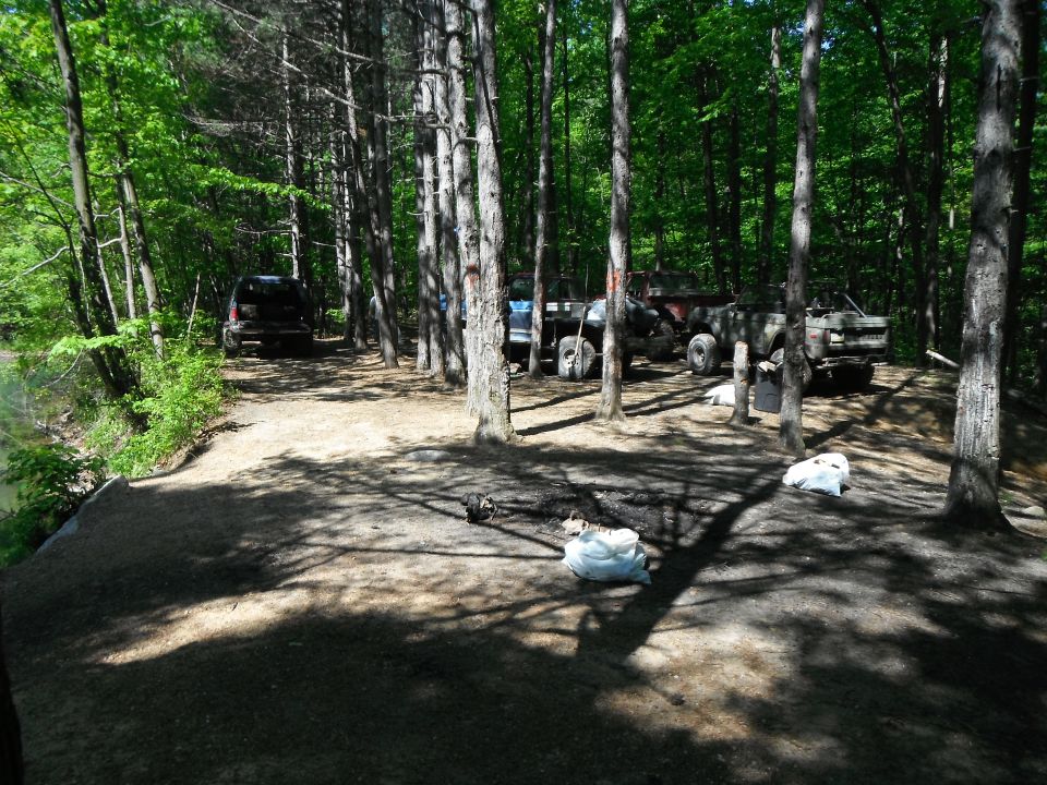 Several trucks and SUVs parked in a wooded area near a body of water
