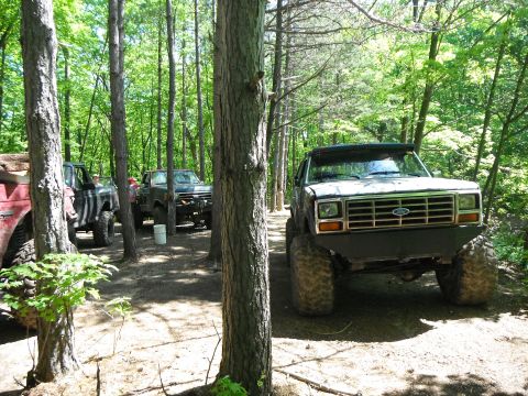 1988 Ford Bronco - Several off-road vehicles are parked in a wooded area.