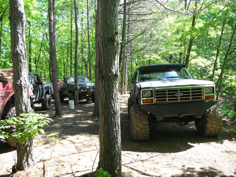 Modified Ford Bronco with large tires and custom bumper parked on dirt path