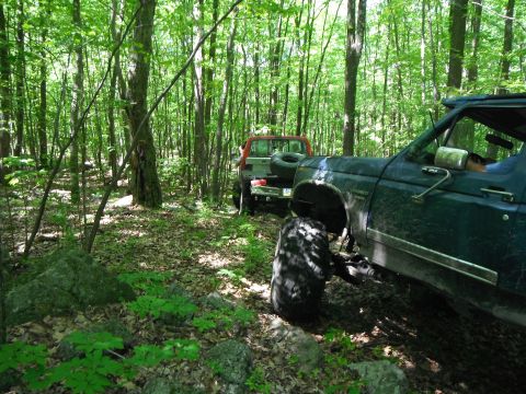1988 Ford Bronco - Two off-road vehicles navigate a wooded trail during a cleanup event.