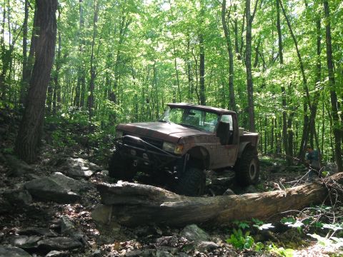 1988 Ford Bronco - A red 1988 Ford Bronco tackles a challenging rocky path through a dense forest.