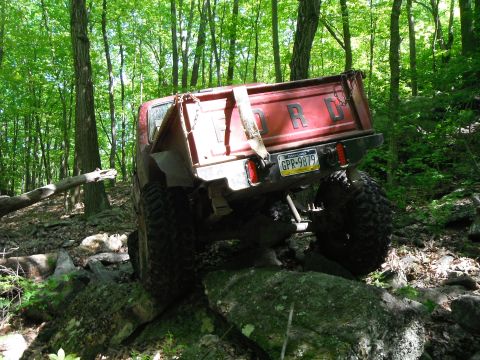 1988 Ford Bronco - Ford pickup truck with large tires off-roading on a rocky, wooded trail.