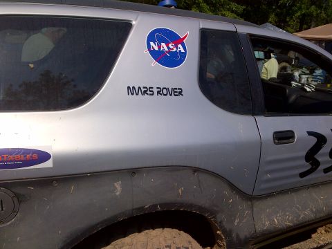1999 Isuzu Vehicross - A silver SUV, marked as a 'Mars Rover' with NASA decals, is seen from the side, covered in mud.