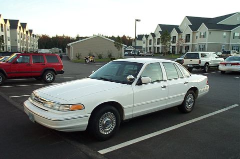 1991 Ford LTD Crown Victoria - Front three-quarter view of a white 1990s aero-body Ford Crown Victoria four-door sedan with lace-style alloy wheel covers and a chrome A-p…