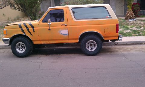 1990 Ford Bronco - This orange Ford Bronco has tiger claw decals on the front fender and primer spots on the driver's door.
