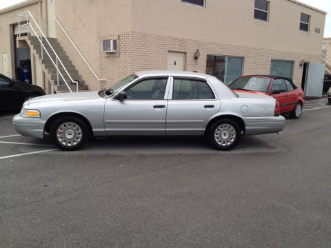 2005 Ford Crown Victoria - A silver 2005 Ford Crown Victoria sedan is parked next to a red convertible.