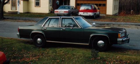 1991 Ford LTD Crown Victoria - A dark green sedan is parked on the side of the road in front of a house with two other vehicles in the driveway.
