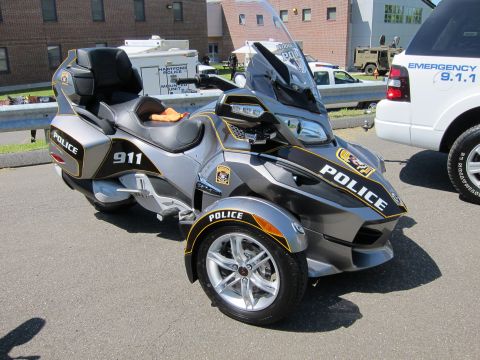 1991 Ford LTD Crown Victoria - Silver three-wheeled Can-Am Spyder police trike marked POLICE and 911 with a rear top case, parked in a lot.