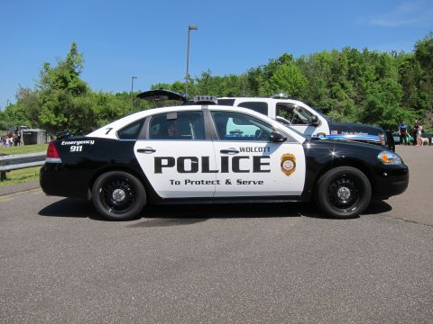 1991 Ford LTD Crown Victoria - Side profile of a black-and-white Wolcott Police Chevrolet Impala cruiser, To Protect and Serve, in a lot.