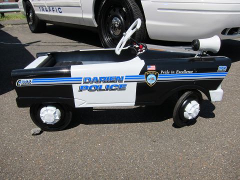 1991 Ford LTD Crown Victoria - small Darien Police pedal car toy in black-and-white livery with a megaphone, parked beside a real cruiser.