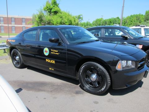 1991 Ford LTD Crown Victoria - black Beacon Falls Police Dodge Charger with gold lettering and seal parked among other police vehicles.