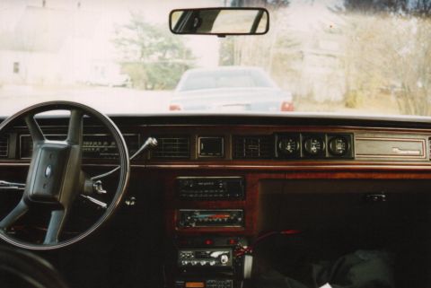 1991 Ford LTD Crown Victoria - Driver's-eye dash view inside a boxy 1980s Ford full-size sedan, showing the two-spoke steering wheel, woodgrain-trimmed dash, round rotary…