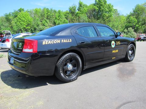 1991 Ford LTD Crown Victoria - black Dodge Charger sedan lettered BEACON FALLS POLICE sits on pavement, viewed from the rear passenger side.