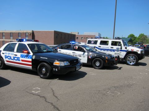 1991 Ford LTD Crown Victoria - Several modern police cars lined up in a parking lot, including a stars-and-stripes-wrapped New Britain sedan and a black SUV.