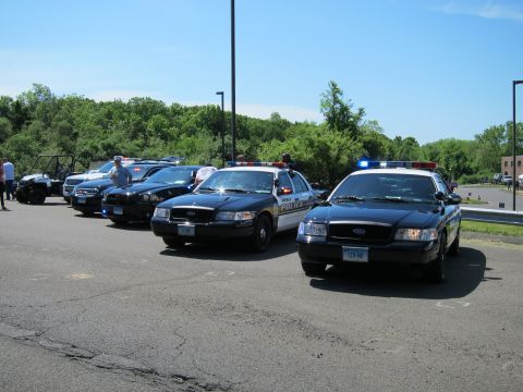1991 Ford LTD Crown Victoria - Several black Ford Crown Victoria police sedans with light bars angled in a parking lot beneath a clear blue sky.