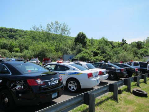 1991 Ford LTD Crown Victoria - Modern police cars lined up along a guardrail in a lot, a black Ford Taurus and white Dodge Charger nearest the camera.
