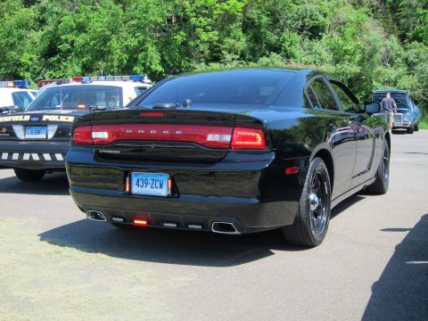 1991 Ford LTD Crown Victoria - black Dodge Charger photographed from behind showing badge and Connecticut plate 439-ZCW, other cruisers at left.