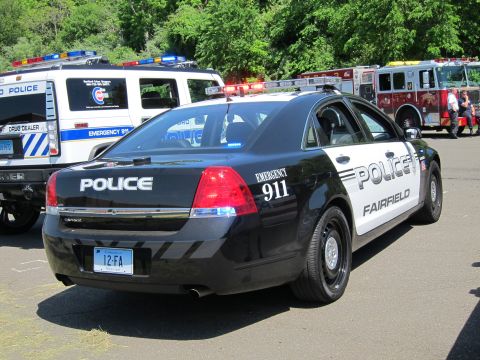 1991 Ford LTD Crown Victoria - black-and-white Chevrolet Caprice sedan lettered FAIRFIELD POLICE EMERGENCY 911 seen from the rear, fire truck behind.