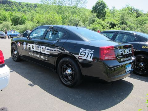 1991 Ford LTD Crown Victoria - black Dodge Charger sedan lettered POLICE NEW FAIRFIELD EMERGENCY 911 with steel wheels parked among other cruisers.