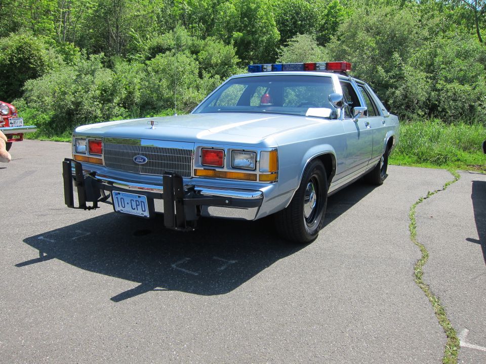 Light-blue 1980s Ford LTD Crown Victoria police sedan with push bar, front three-quarter