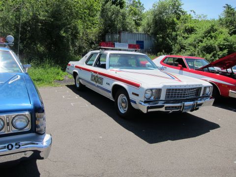 1991 Ford LTD Crown Victoria - white striped Plymouth Fury police sedan parked next to a blue Ford LTD cruiser in a sunny show lot.