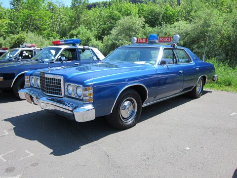 1991 Ford LTD Crown Victoria - blue 1970s Ford LTD lettered STATE POLICE with stacked headlights and red-and-blue roof beacons parked in a show lot.