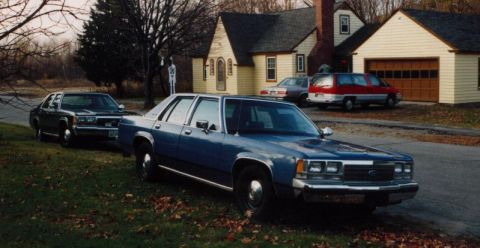 1991 Ford LTD Crown Victoria - Front three-quarter passenger-side view of a blue Ford LTD Crown Victoria sedan parked on a leaf-covered lawn with no front plate and bare…