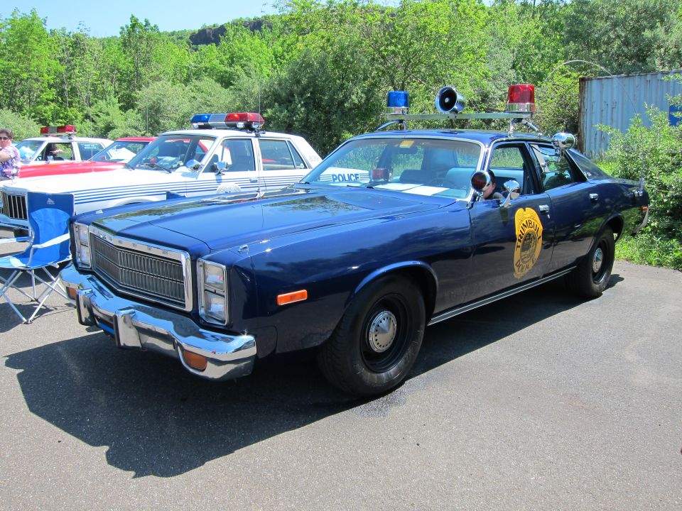 Dark blue vintage police sedan with roof siren and lightbar at a car show