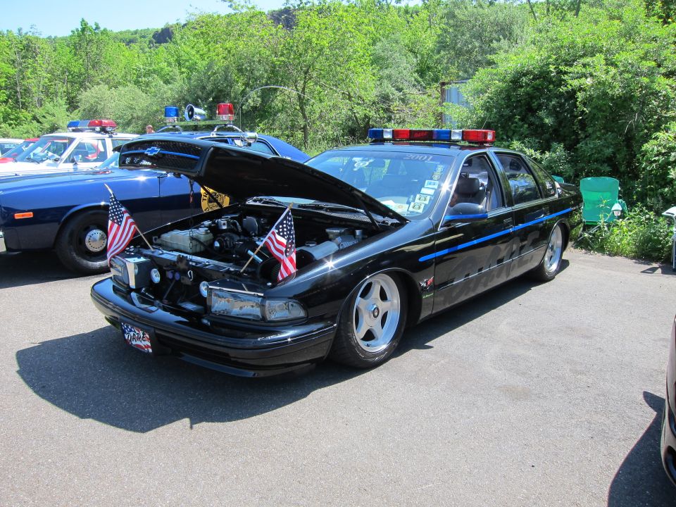Black police sedan with open hood and U.S. flags at a car show
