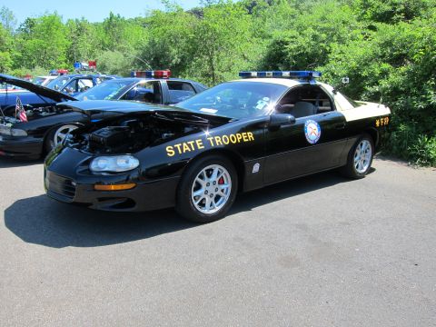 1991 Ford LTD Crown Victoria - black-and-tan Camaro marked STATE TROOPER with a roof lightbar and open hood parked at a vehicle show.