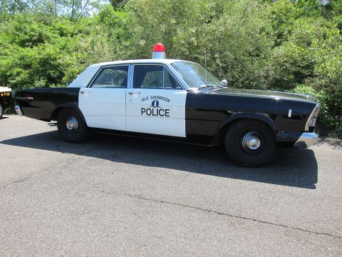 1991 Ford LTD Crown Victoria - black-and-white vintage sedan lettered OLD SAYBROOK POLICE with a single red roof beacon, parked near greenery.