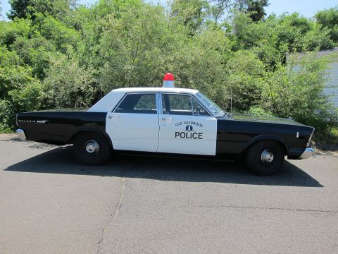 1991 Ford LTD Crown Victoria - Side profile of a black-and-white vintage police sedan lettered OLD SAYBROOK POLICE with a red roof beacon.