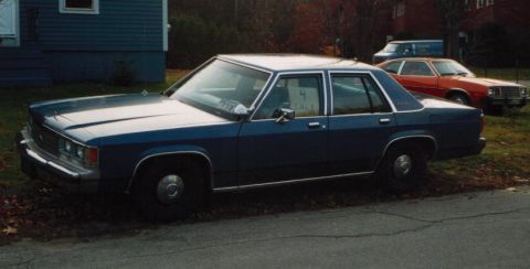 1991 Ford LTD Crown Victoria - Side view of a two-tone blue boxy Ford LTD Crown Victoria four-door sedan on black steel wheels with dog-dish caps, parked on a grassy road…