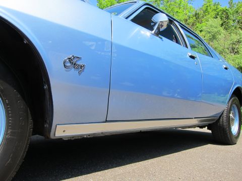1991 Ford LTD Crown Victoria - Close-up of a light blue car's front fender and door showing a chrome Fury script badge and rocker trim.