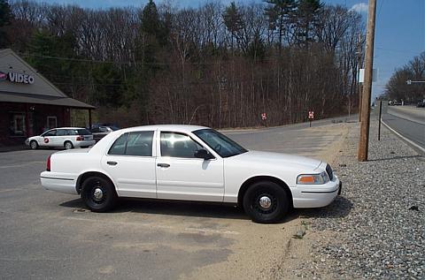 1991 Ford LTD Crown Victoria - A white sedan is parked on the side of the road near a building with a "VIDEO" sign.