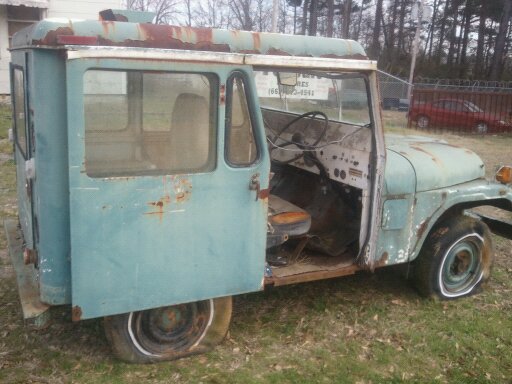 Old teal Jeep panel van with flat tires and rust, driver's door open