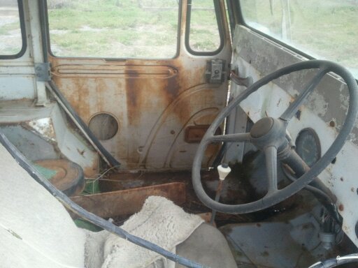 Rusty interior of an old vehicle with a large steering wheel and worn seats
