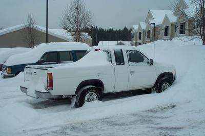 1991 Ford LTD Crown Victoria - Rear three-quarter view of a white extended-cab compact pickup snowed in at a residential parking lot, its bed and roof coated with several…