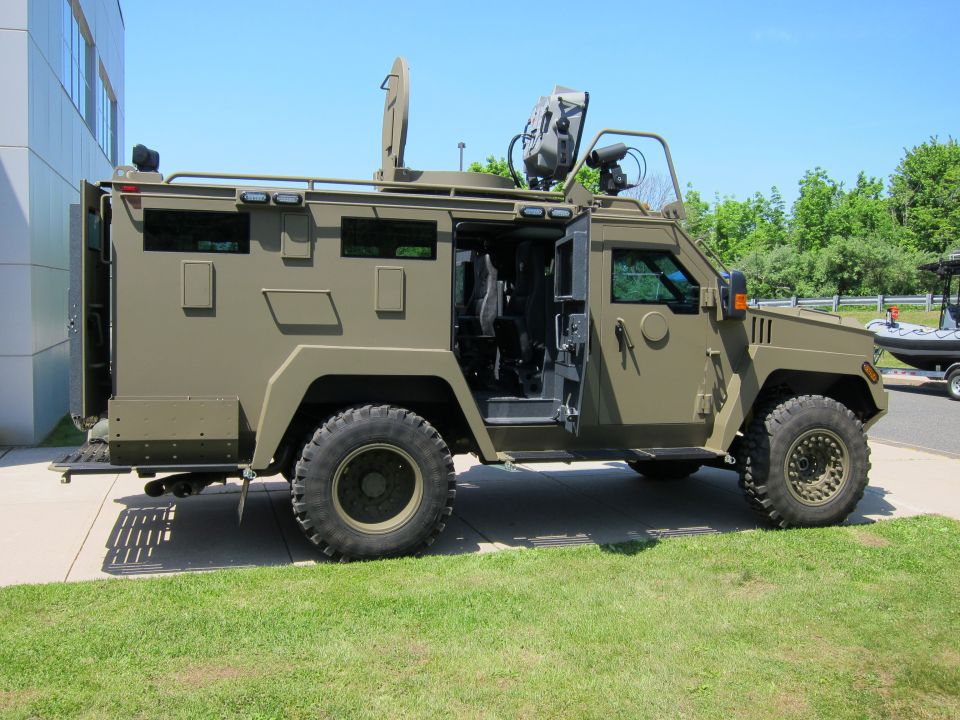 Side view of olive-green armored truck with open door and roof-mounted optics