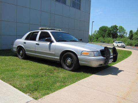 1991 Ford LTD Crown Victoria - silver Ford Crown Victoria police interceptor with light bar and front push bumper parked on grass beside a tiled building.