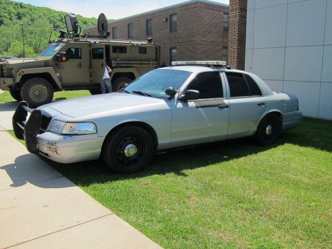 1991 Ford LTD Crown Victoria - silver Ford Crown Victoria police cruiser parked on grass with a tan armored tactical vehicle behind it.