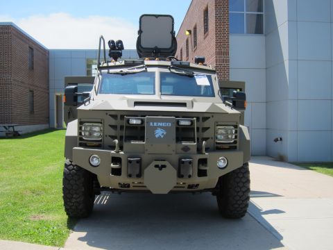 1991 Ford LTD Crown Victoria - Head-on view of a tan-green Lenco armored vehicle with a roof-mounted optics screen and heavy front grille guard.