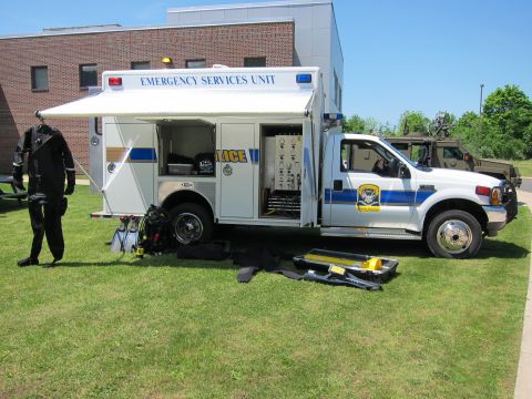 1991 Ford LTD Crown Victoria - white Emergency Services Unit utility truck with rear compartment open, a black diving dry suit and gear laid out beside it.