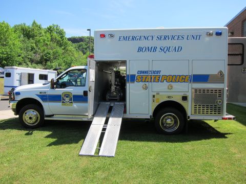 1991 Ford LTD Crown Victoria - white Connecticut State Police Emergency Services Unit Bomb Squad box truck with a metal loading ramp deployed on grass.