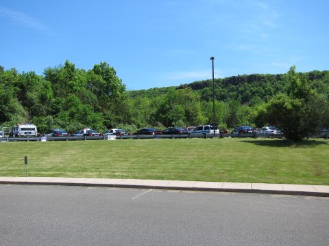 1991 Ford LTD Crown Victoria - grassy field with a far-off line of parked vehicles along a roadside guardrail beneath a green wooded hillside.